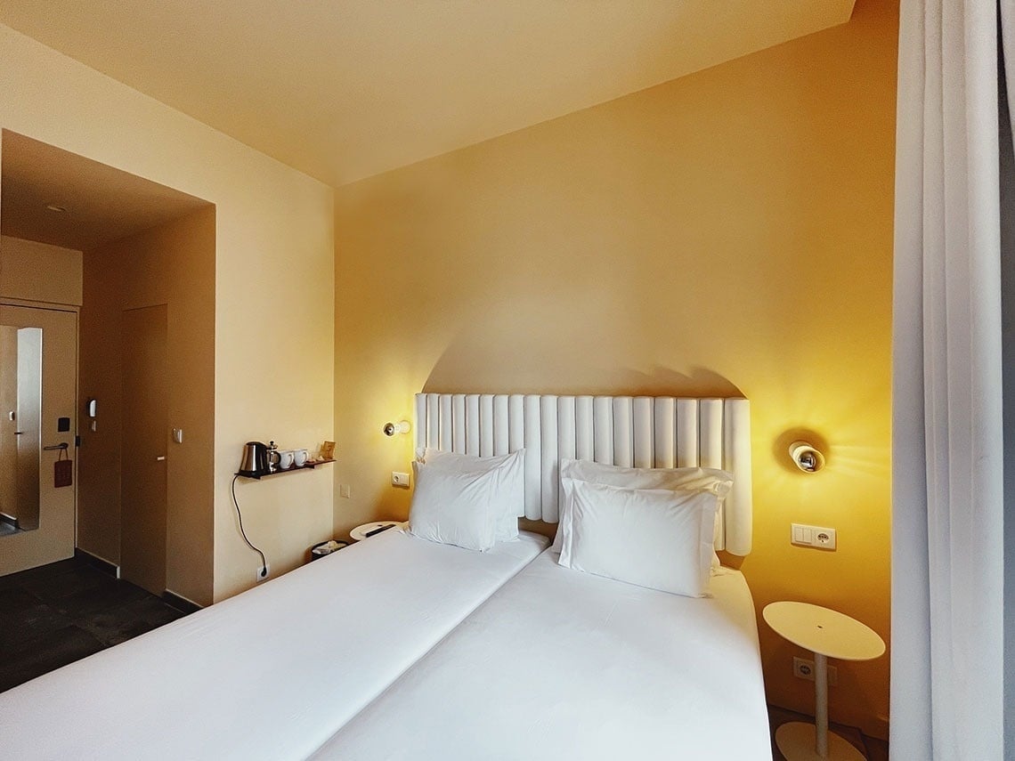 TEST3: Copia 4 - Quarto de hotel moderno com duas camas brancas e paredes amarelas.