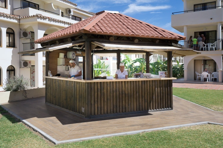 two people standing behind a wooden bar with a red tile roof