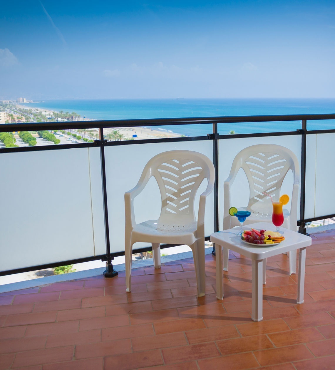 ein weißer Plastikstuhl sitzt auf einem Balkon neben einem kleinen Tisch mit einem Cocktail darauf