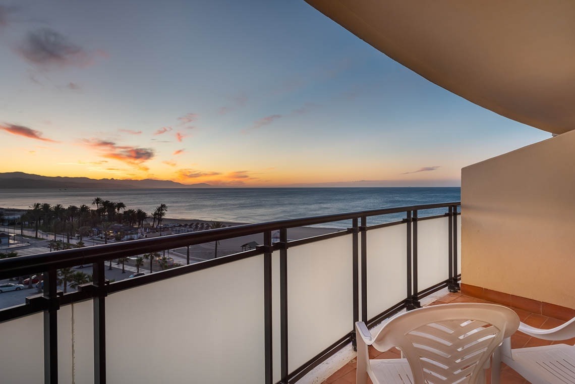un balcon avec une chaise et une vue sur l' océan au coucher du soleil