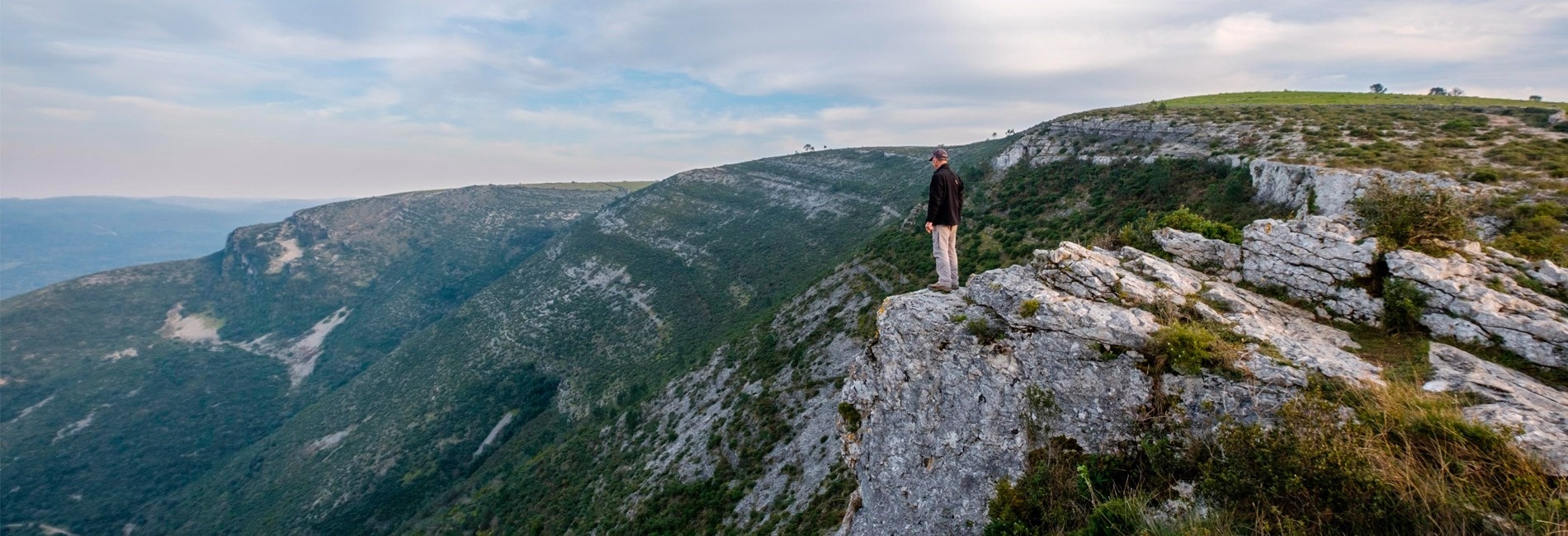 a man stands on a rocky cliff overlooking a valley