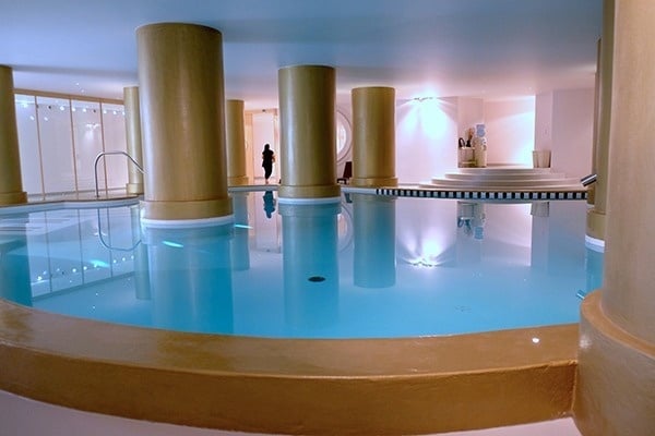 Une piscine intérieure lumineuse avec un revêtement de sol en bois, des couloirs de nage et des chaises jaunes le long du mur.
