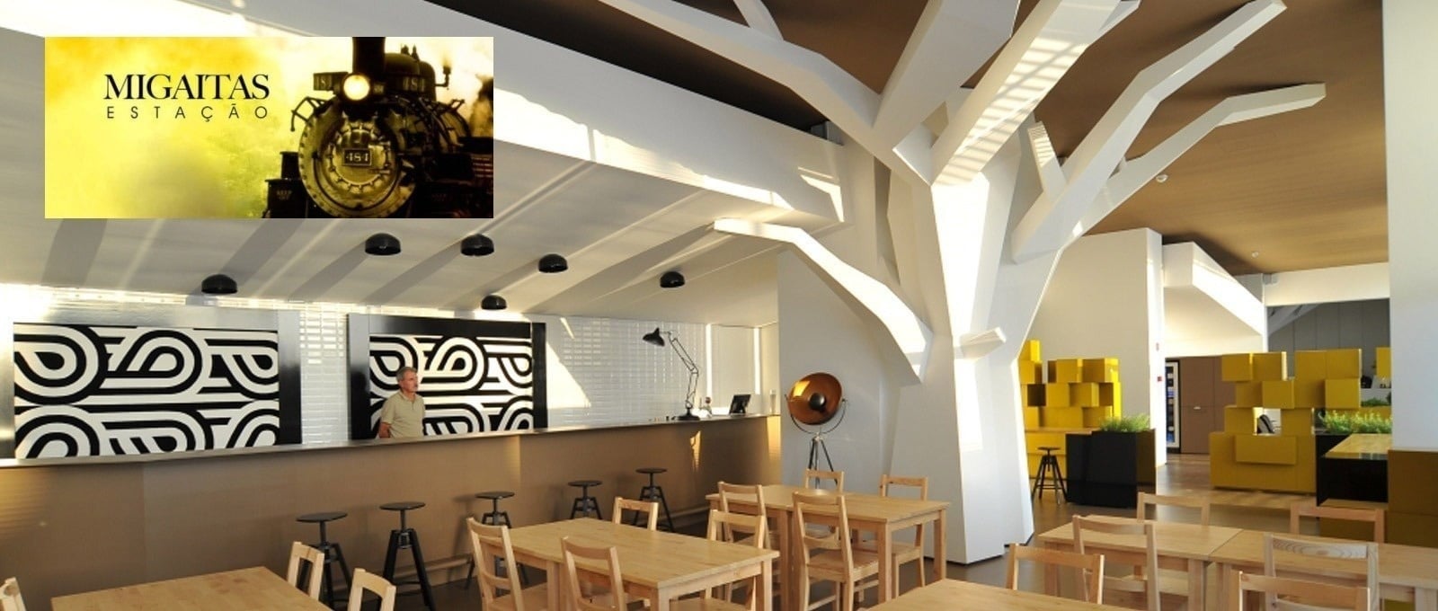 Une salle de restaurant lumineuse et élégante avec de nombreuses tables dressées est visible à travers de grandes baies vitrées donnant sur une végétation luxuriante et ensoleillée.