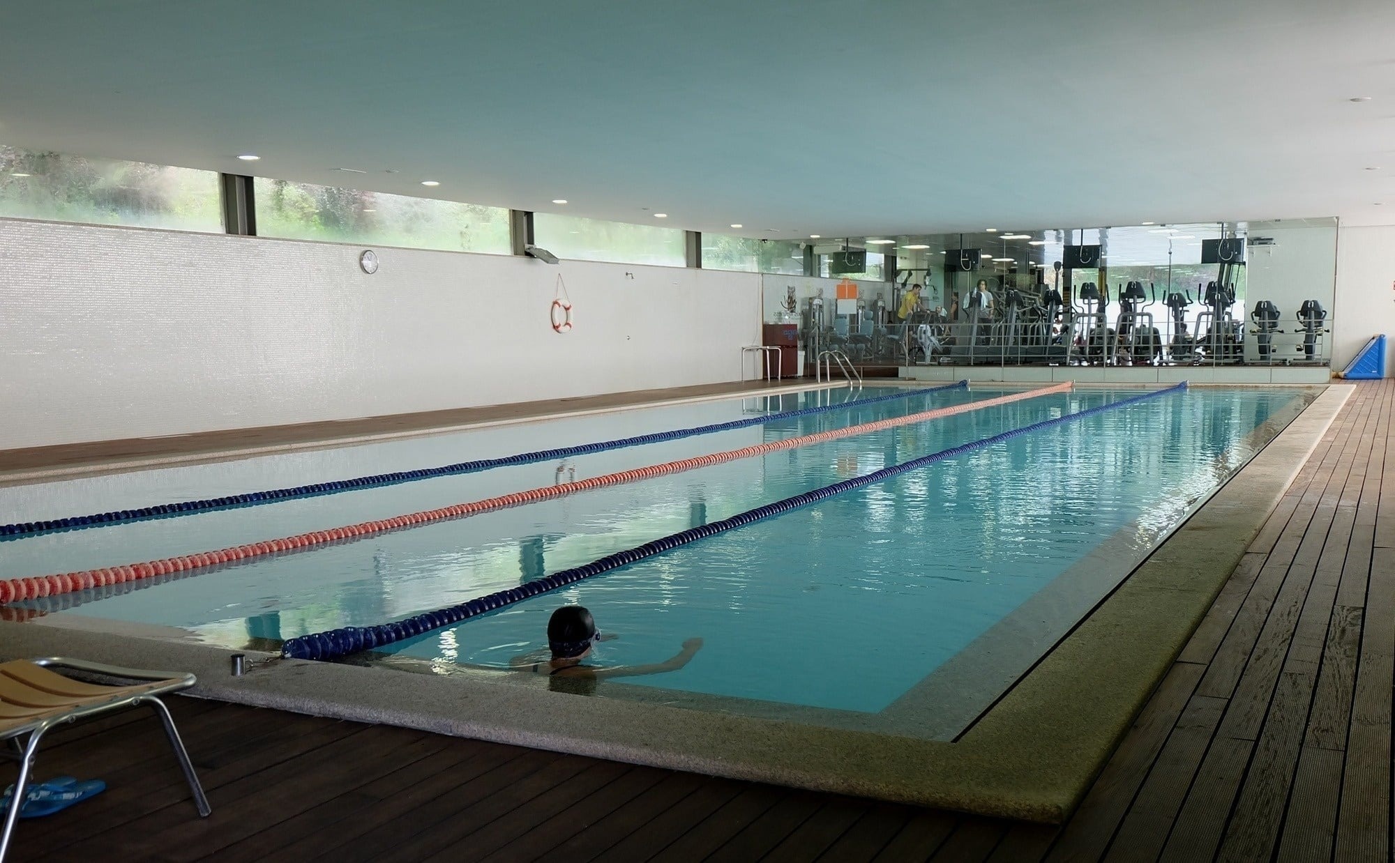 Une piscine intérieure lumineuse avec un revêtement de sol en bois, des couloirs de nage et des chaises jaunes le long du mur.