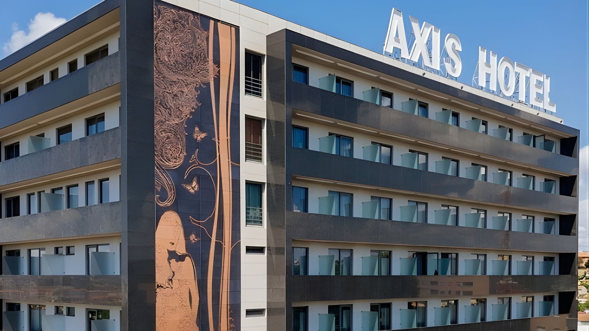 L'image montre la façade d'un hôtel moderne, l'Axis Hotel, arborant une grande fresque murale artistique et de nombreux balcons.
