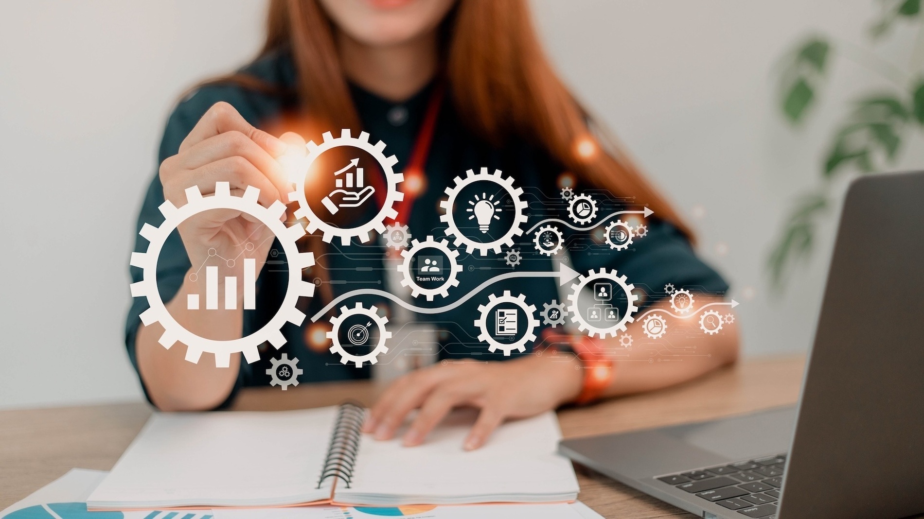 a woman is sitting at a desk using a laptop and drawing gears and icons