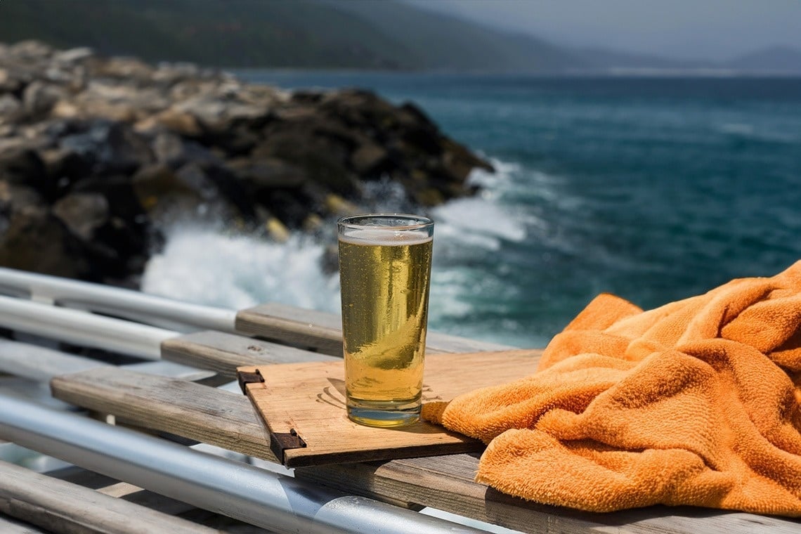 a tall glass of beer sits on a wooden cutting board
