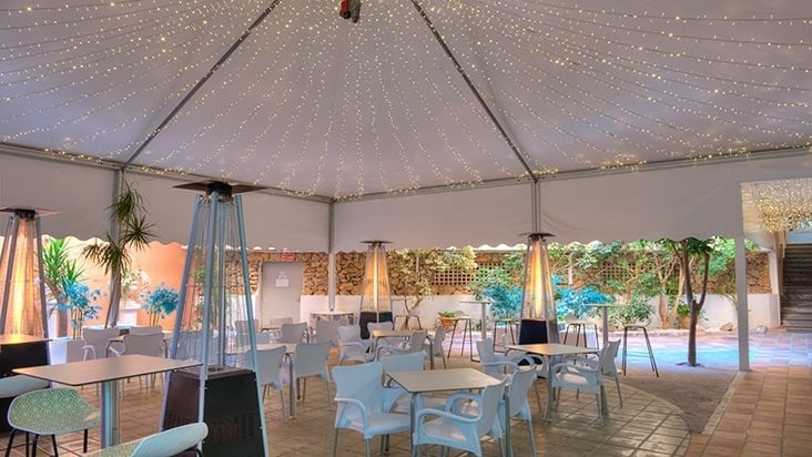 tables and chairs under a tent with lights on the ceiling