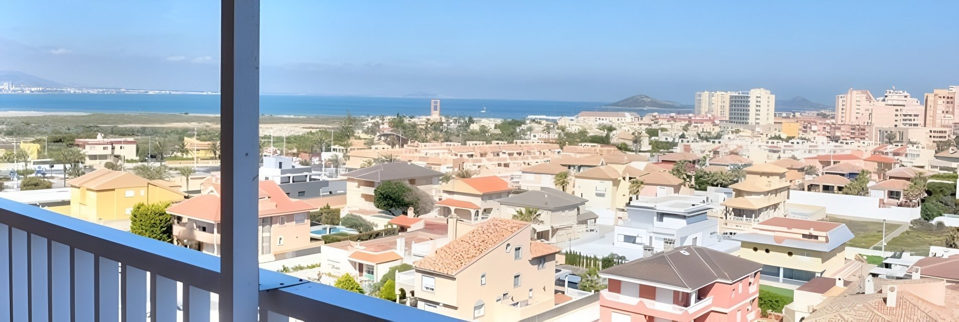 a view of a city from a balcony with the ocean in the background