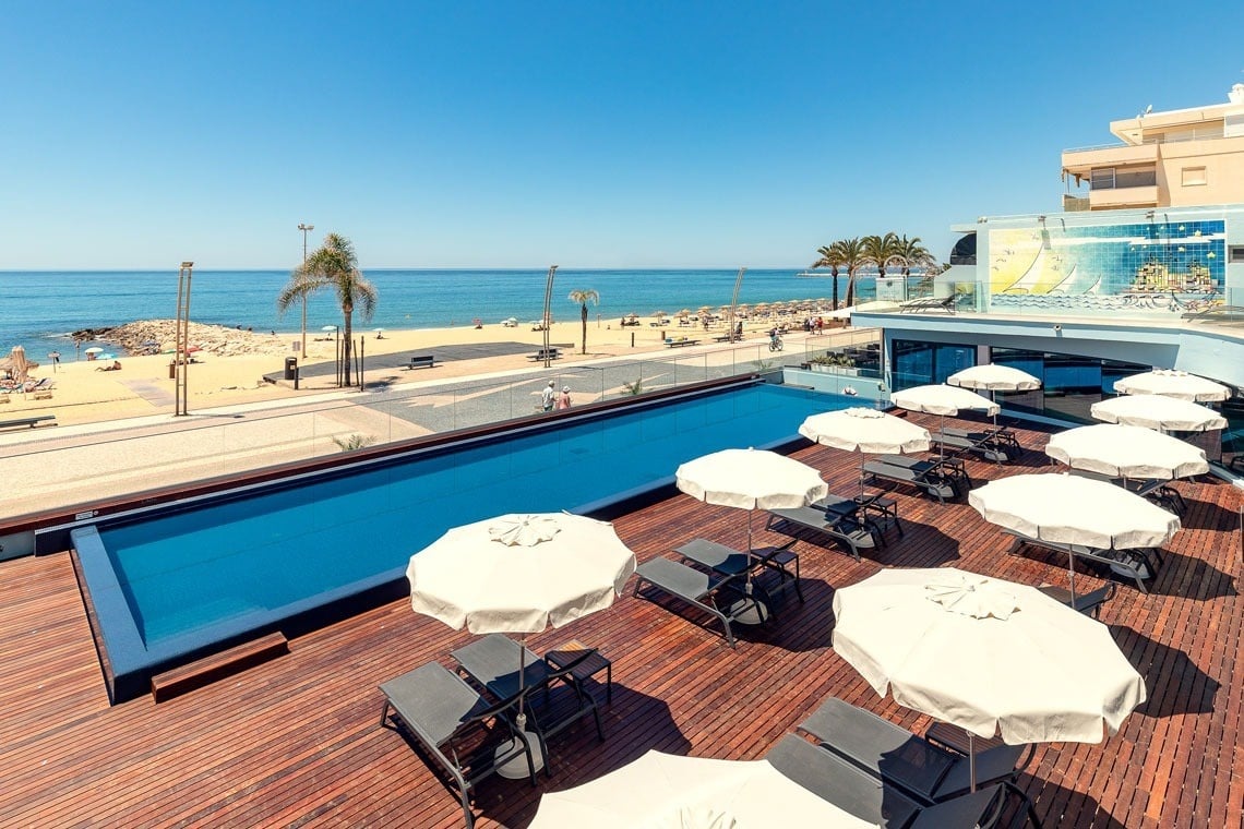 uma grande piscina cercada por guarda-sóis e cadeiras com vista para o oceano