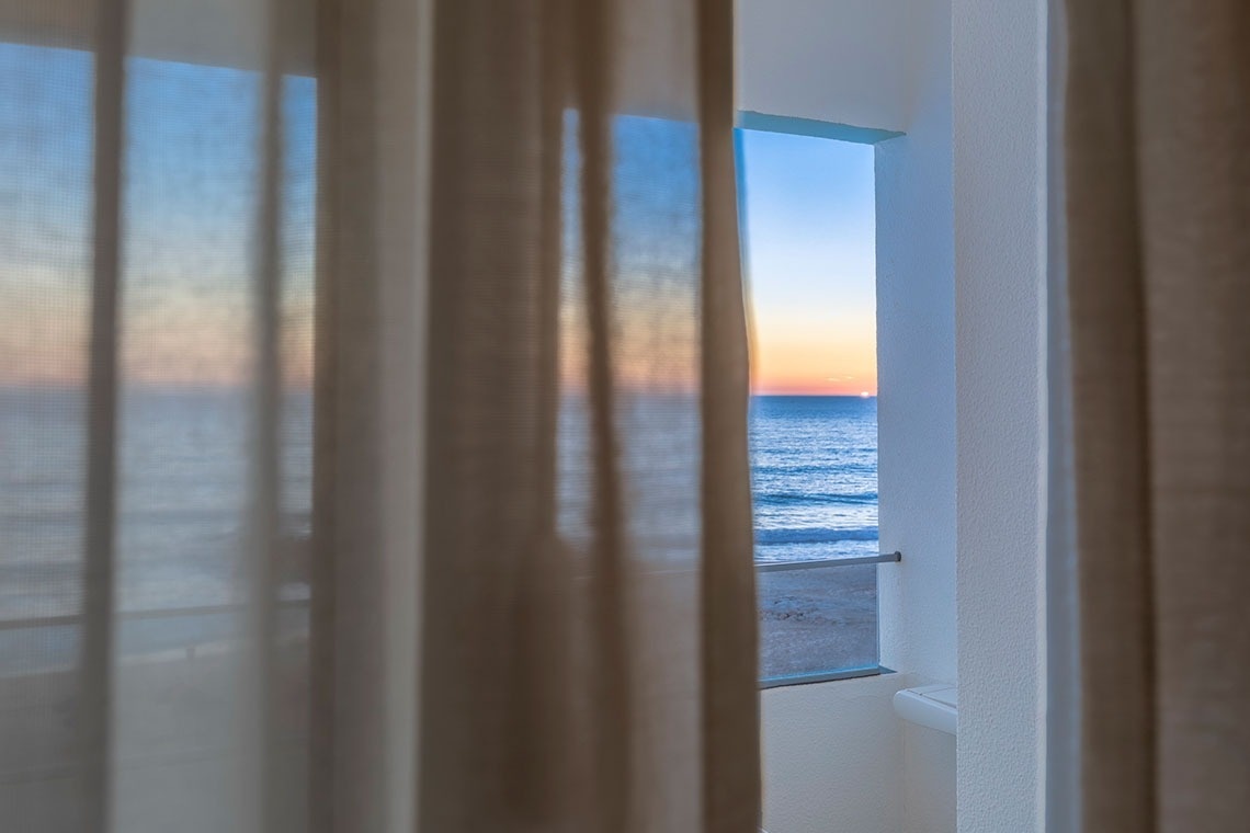 uma janela com vista para o oceano ao pôr do sol
