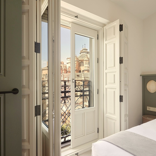 Puerta de balcón abierta con vista a edificios históricos y una cama. U-Sense Granada Gran Vía