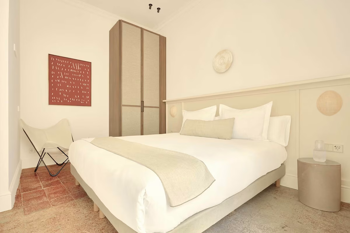 Cama cómoda en habitación de hotel con U-Sense Sevilla Santa Cruz | Apartamentos Turísticos en Sevilla, armario y silla.