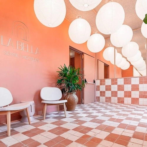 Luminoso lobby de hotel con paredes color coral, sillas blancas y suelo de baldosas a cuadros. U-Sense Granada Centro