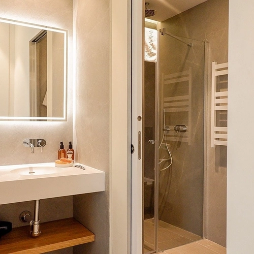 Modern bathroom with illuminated mirror, sink, and shower stall. U-Sense Sevilla Catedral
