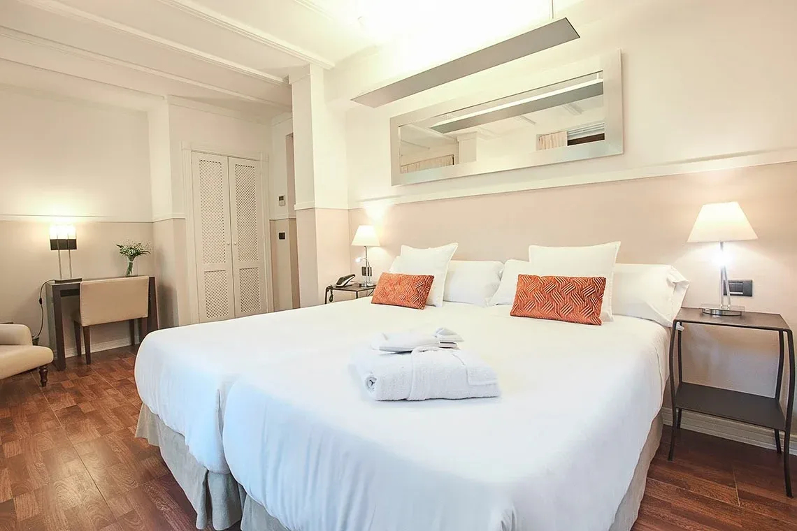 Habitación con dos camas gemelas, almohadas decorativas naranjas y espejo grande sobre la cama. U-Sense Sevilla Centro