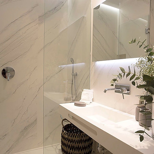 Baño moderno con paredes de mármol, lavabo blanco, ducha y adorno floral. U-Sense Granada Catedral