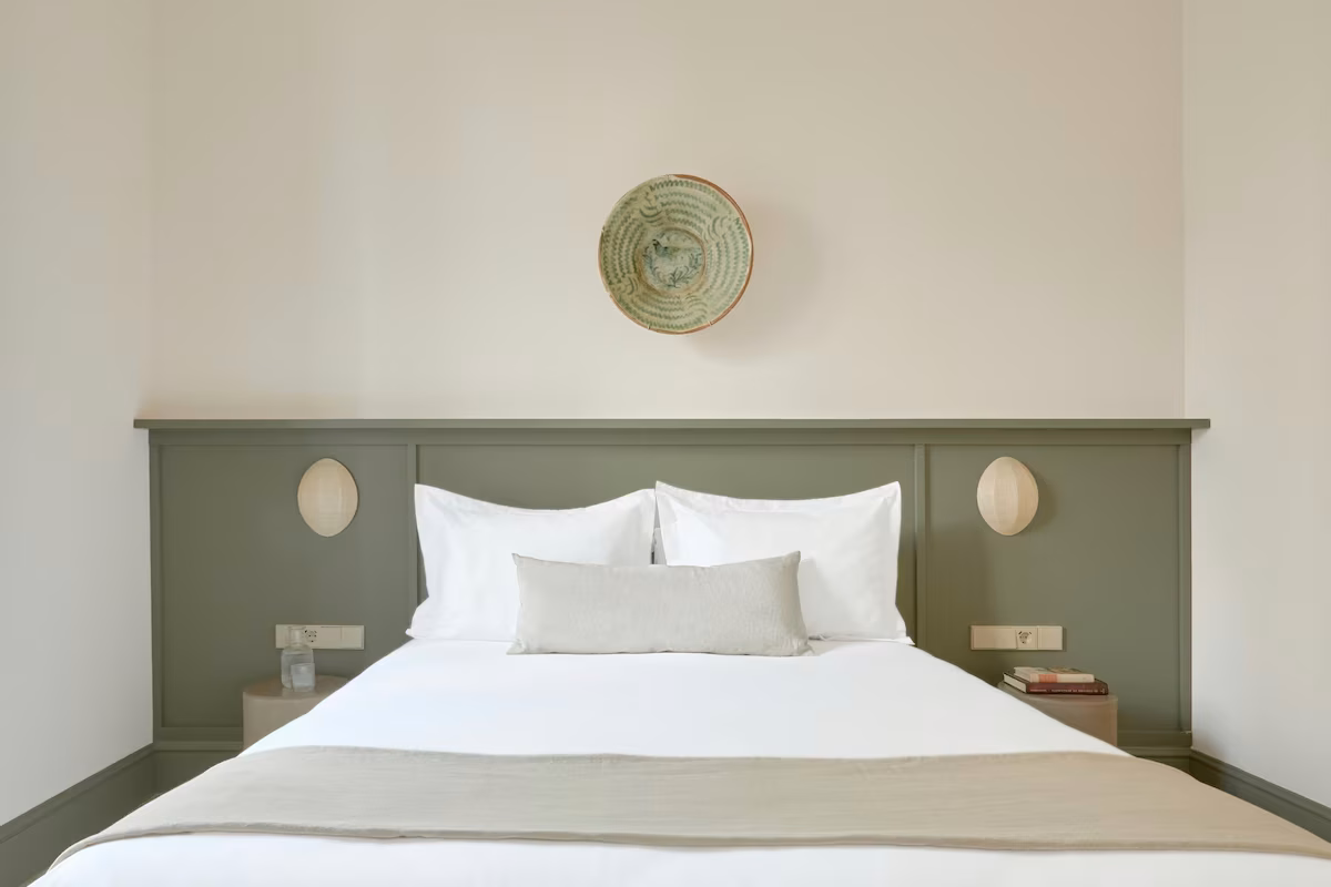 Cozy hotel bedroom with a green headboard, white bedding, and decorative plate. U-Sense