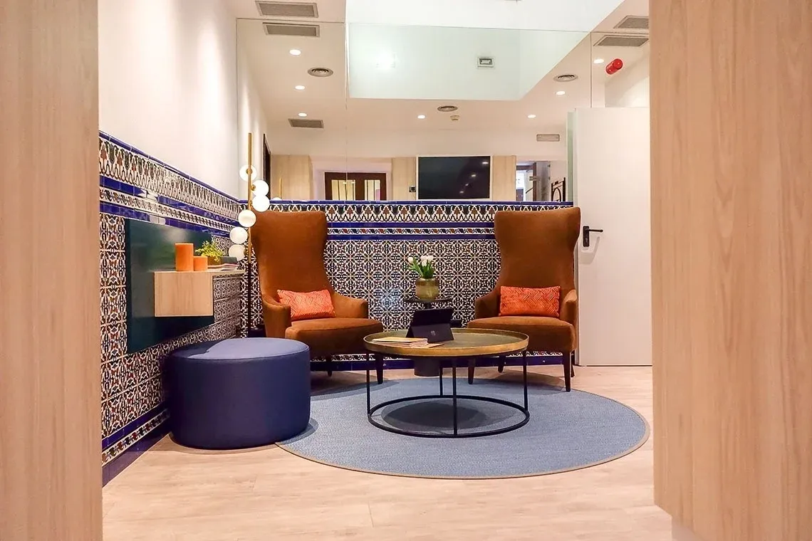 Lobby con sillones elegantes, alfombra azul y azulejos decorativos - U-Sense Sevilla Centro