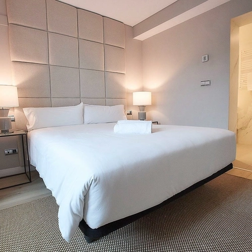 Habitación moderna con cama doble, lámparas de noche y baño adjunto. U-Sense Madrid Santa Ana