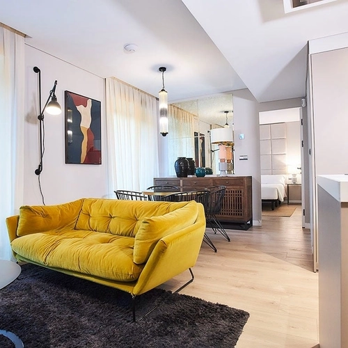 Sofá amarillo en sala de estar con vistas a dormitorio. U-Sense Madrid Santa Ana