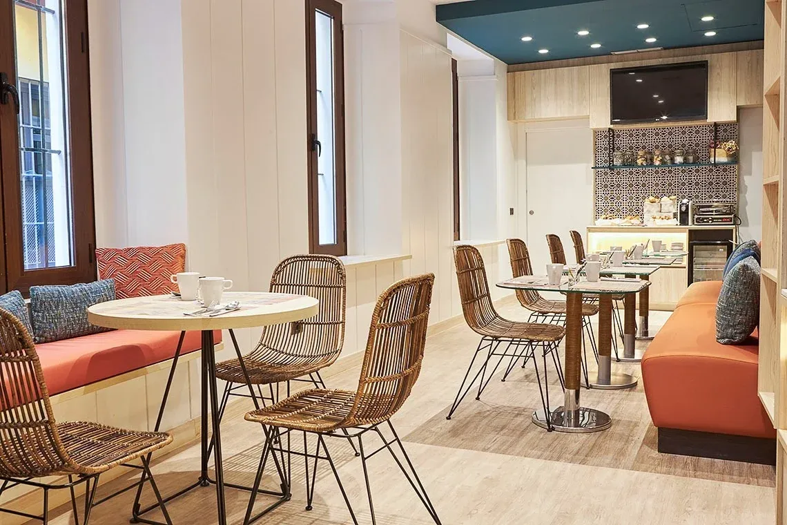 Comedor con mesas de ratán, asientos naranjas y decoración moderna. U-Sense Sevilla Centro