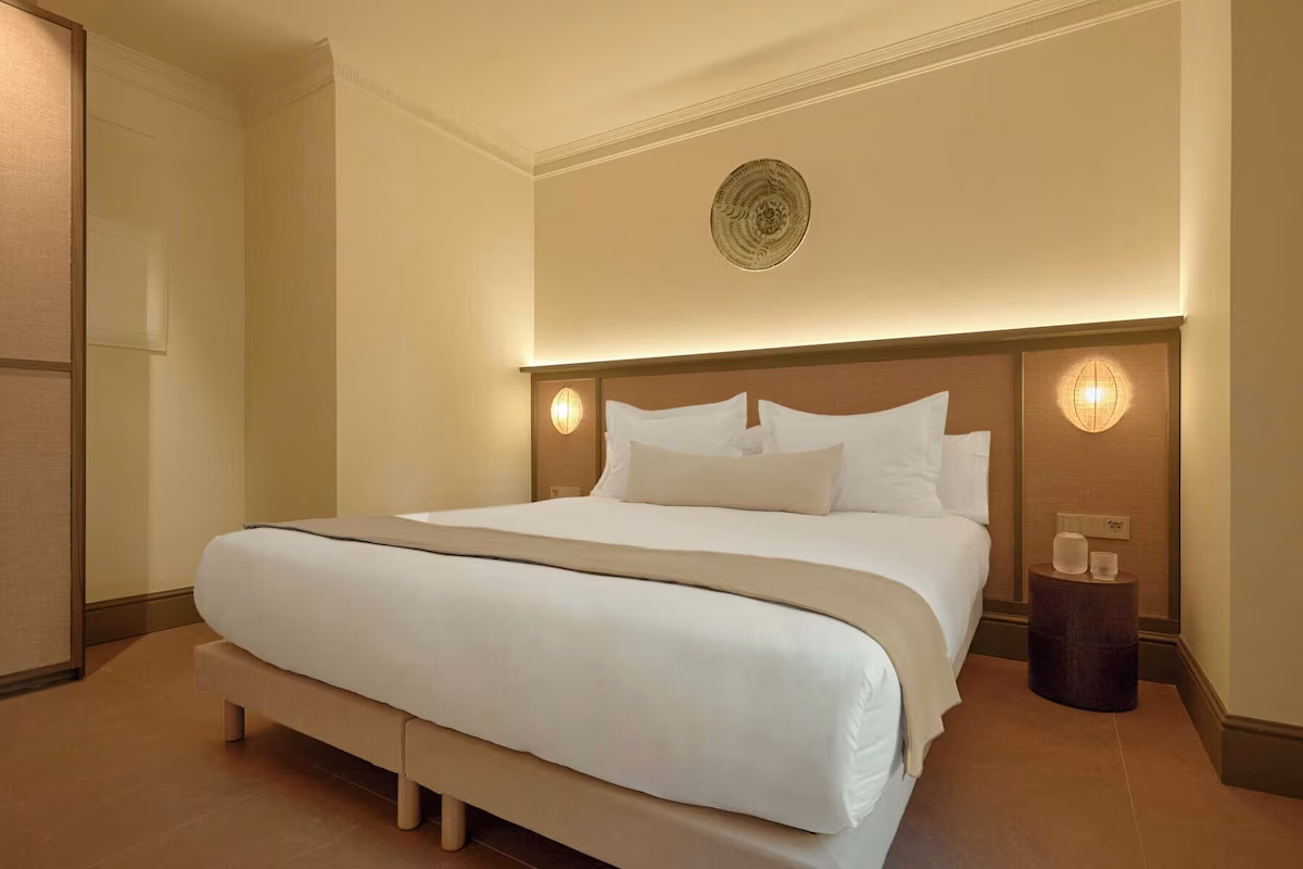 Amplia y luminosa habitación de hotel con cama king size, mesita de noche y lámpara. U-Sense Sevilla Santa Cruz | Apartamentos Turísticos en Sevilla