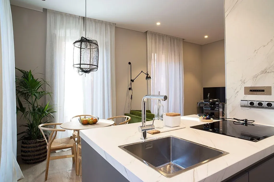Modern open-plan apartment with an island kitchen and a dining area with Wishbone-style chairs and a large indoor plant. U-Sense
