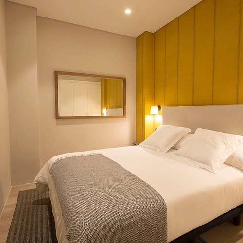 Habitación moderna con cama cómoda y pared amarilla. U-Sense Granada Catedral