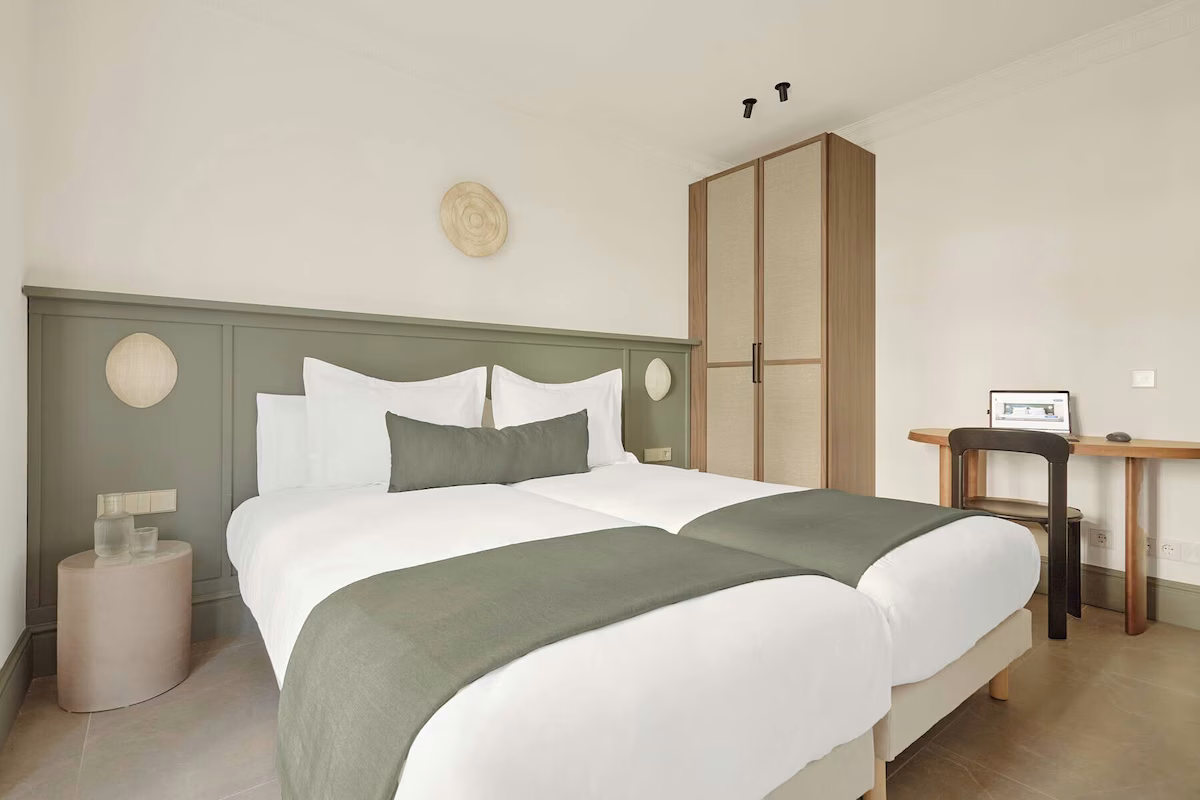 Habitación de hotel con dos camas, escritorio y armario. U-Sense Sevilla Santa Cruz | Apartamentos Turísticos en Sevilla para familias.