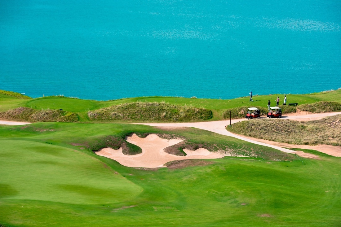 two golf carts are parked on a golf course near the ocean