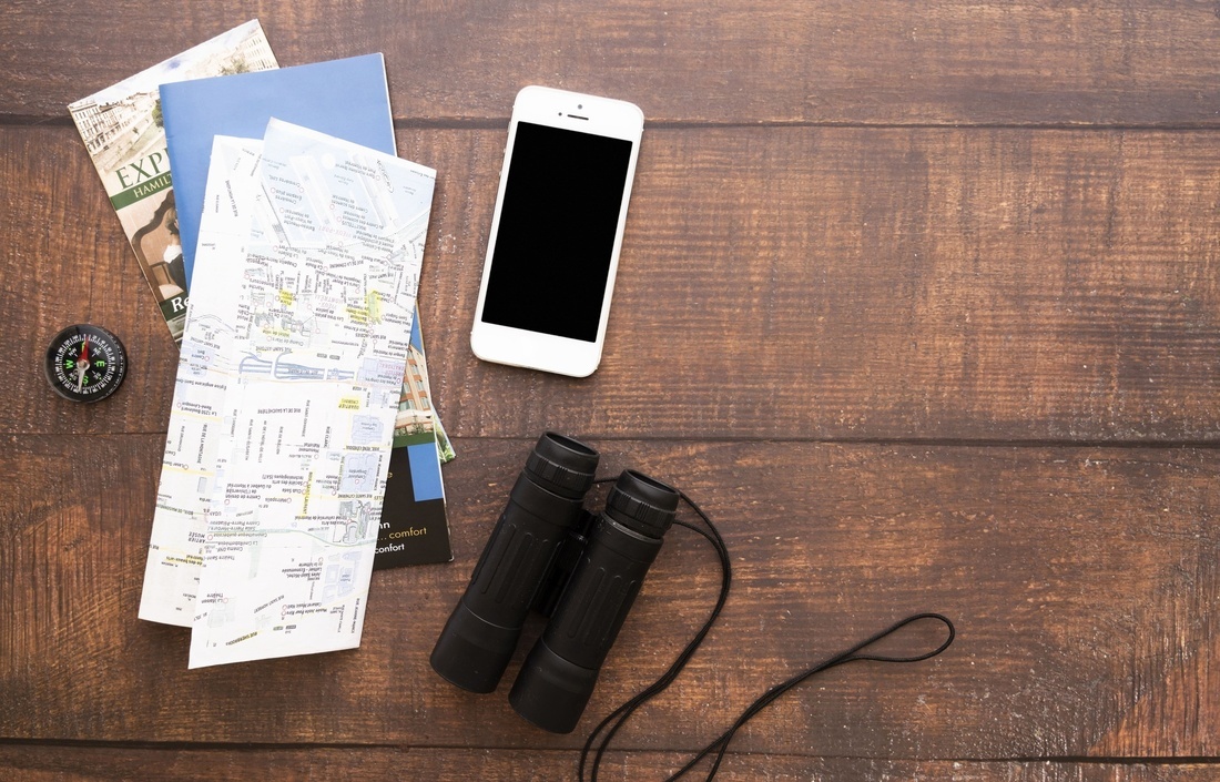 binoculars a cell phone a compass and a map on a wooden table