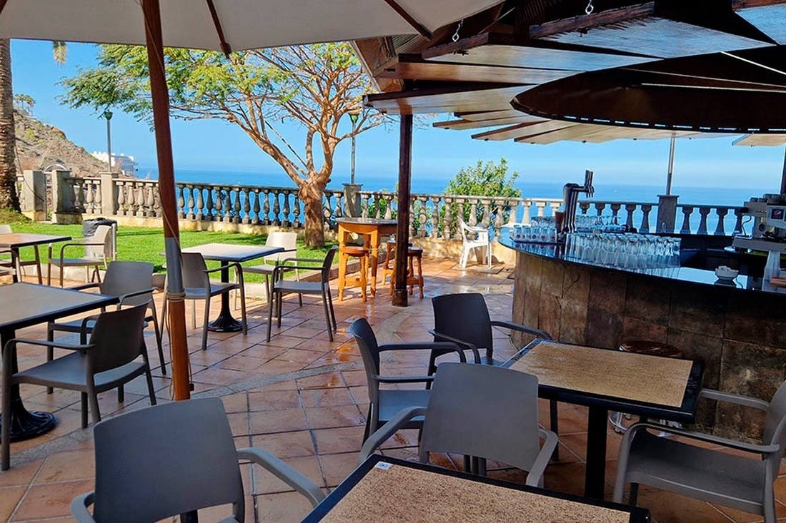 una terraza con mesas y sillas y un bar con vista al océano