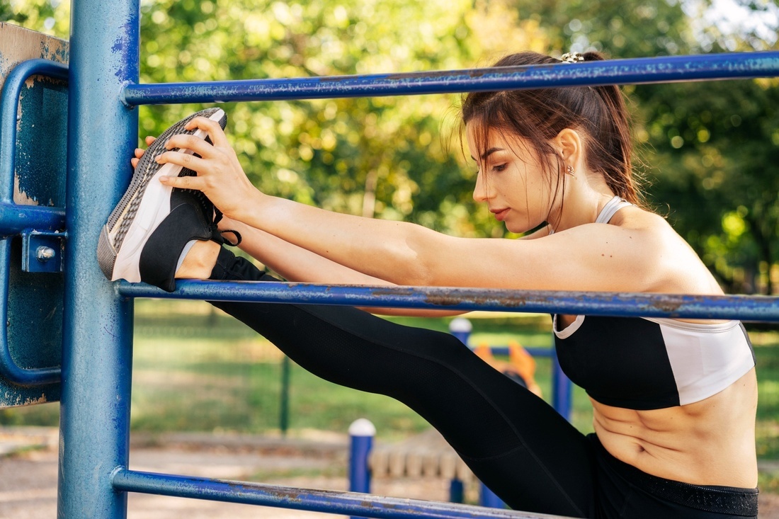 a woman stretches her legs on a metal bar in a park