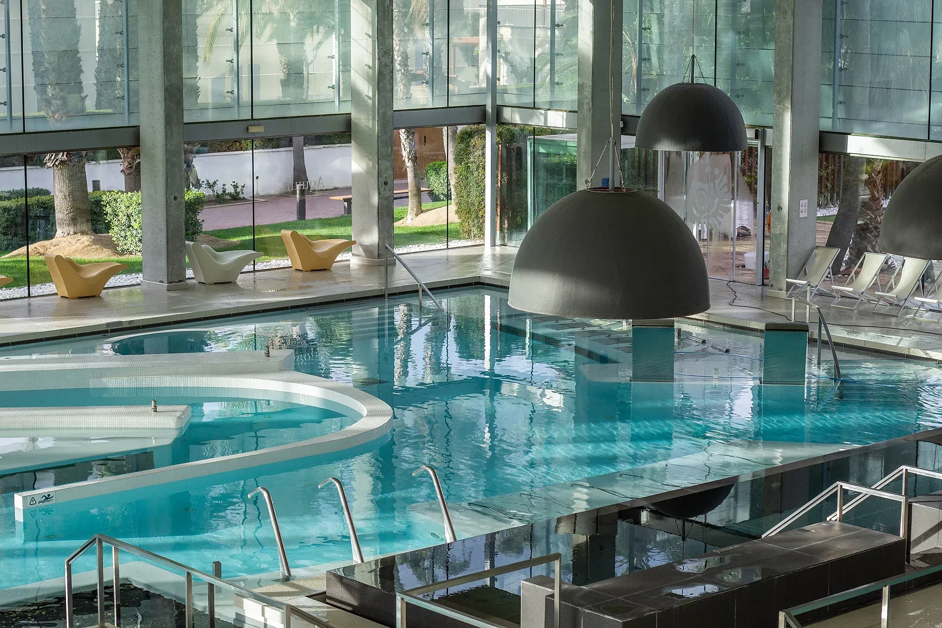 Indoor spa pool with loungers and modern design. Official Aquum Spa & Wellness website.
