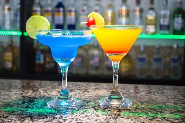 un cóctel azul y un cóctel naranja están sobre un mostrador de bar