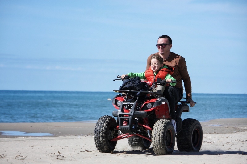 un hombre y un niño montan un atv en la playa