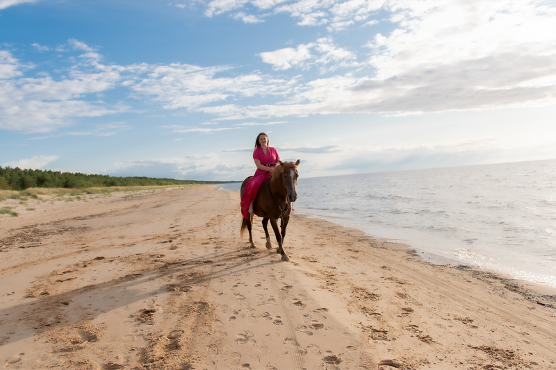 una mujer con un vestido rosa monta un caballo en la playa