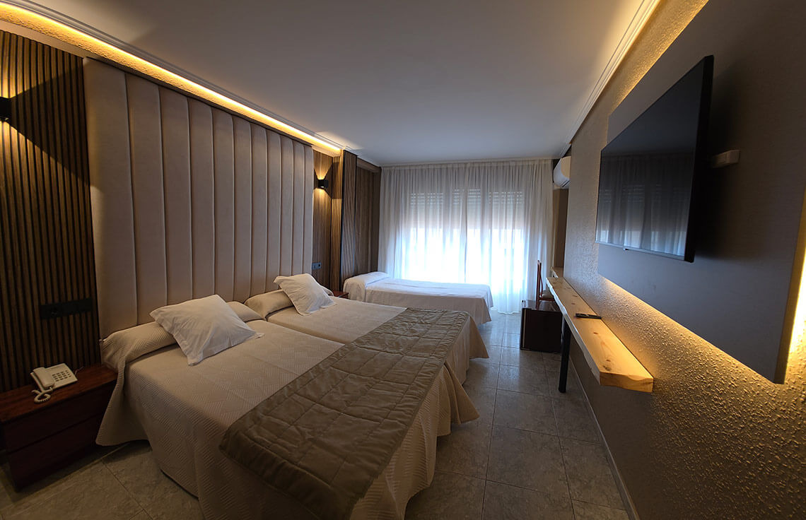 TEST 4 hotel room with three beds, comfortable headboards, and a large TV.