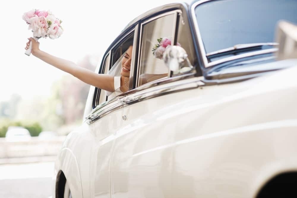 una novia sostiene un ramo de flores mientras mira por la ventana de un coche .