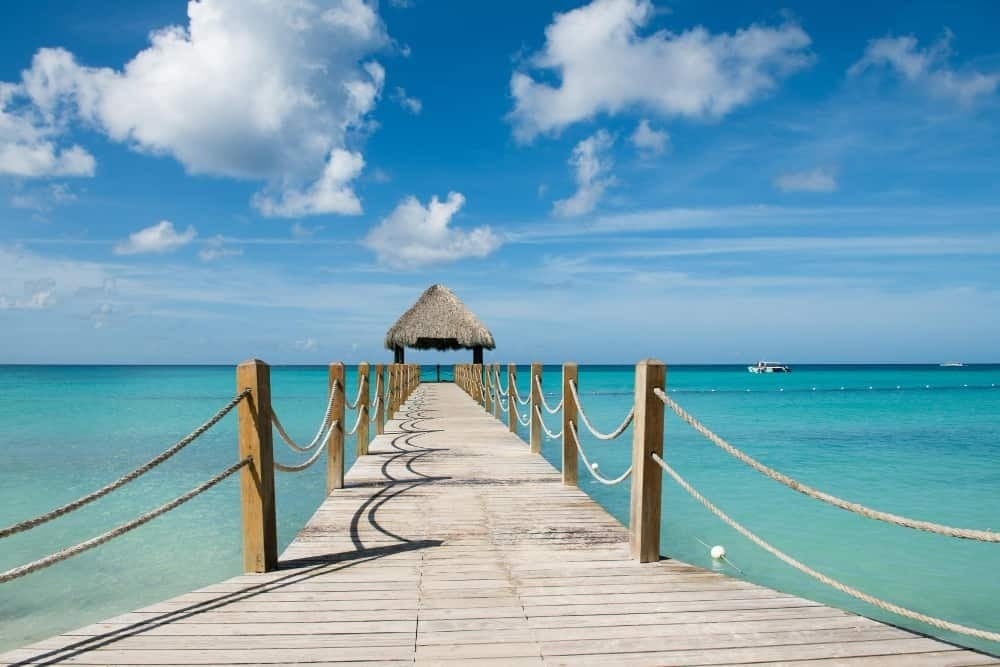a wooden pier leading to the ocean with a thatched hut in the background .