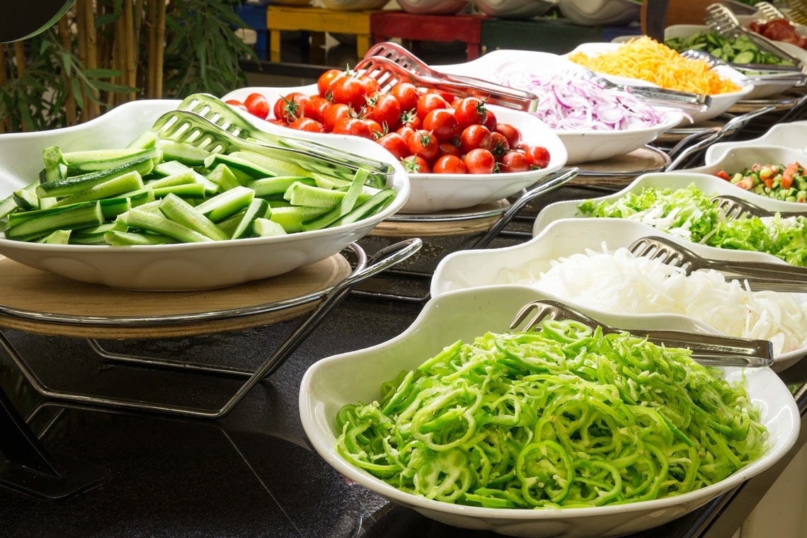 a buffet table with bowls of vegetables including green peppers and tomatoes