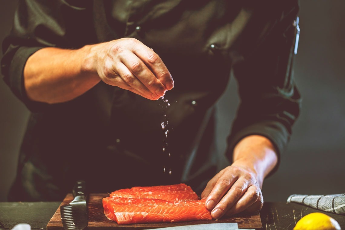 un chef agrega sal a un trozo de pescado en una tabla de cortar