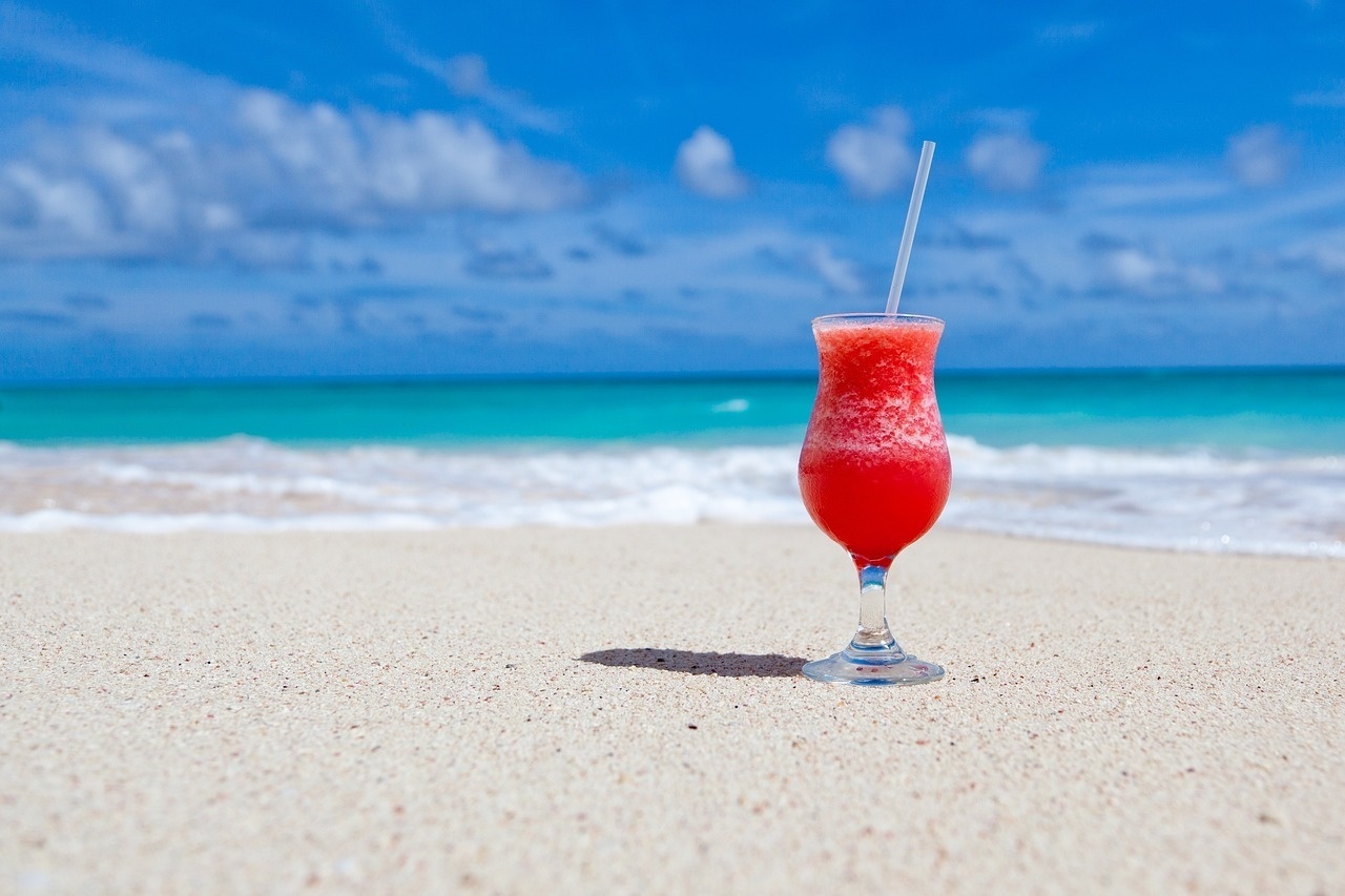 a glass of red liquid with a straw on the beach