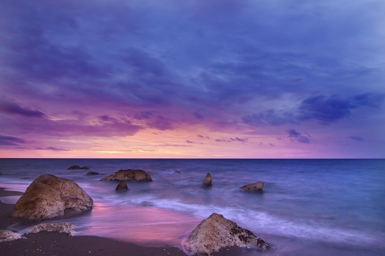 a sunset over the ocean with rocks in the foreground