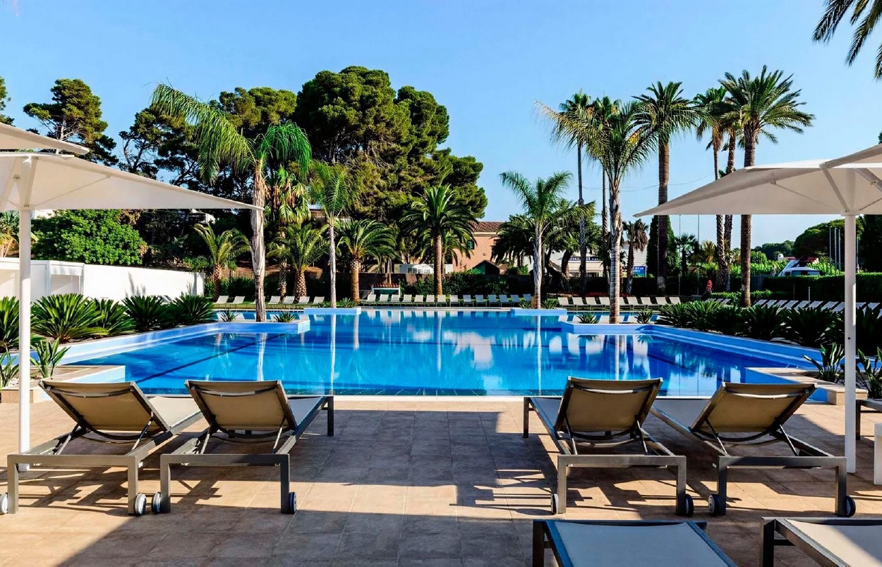 Piscina de hotel y tumbonas con el mar TEST 6 al fondo en un día soleado.
