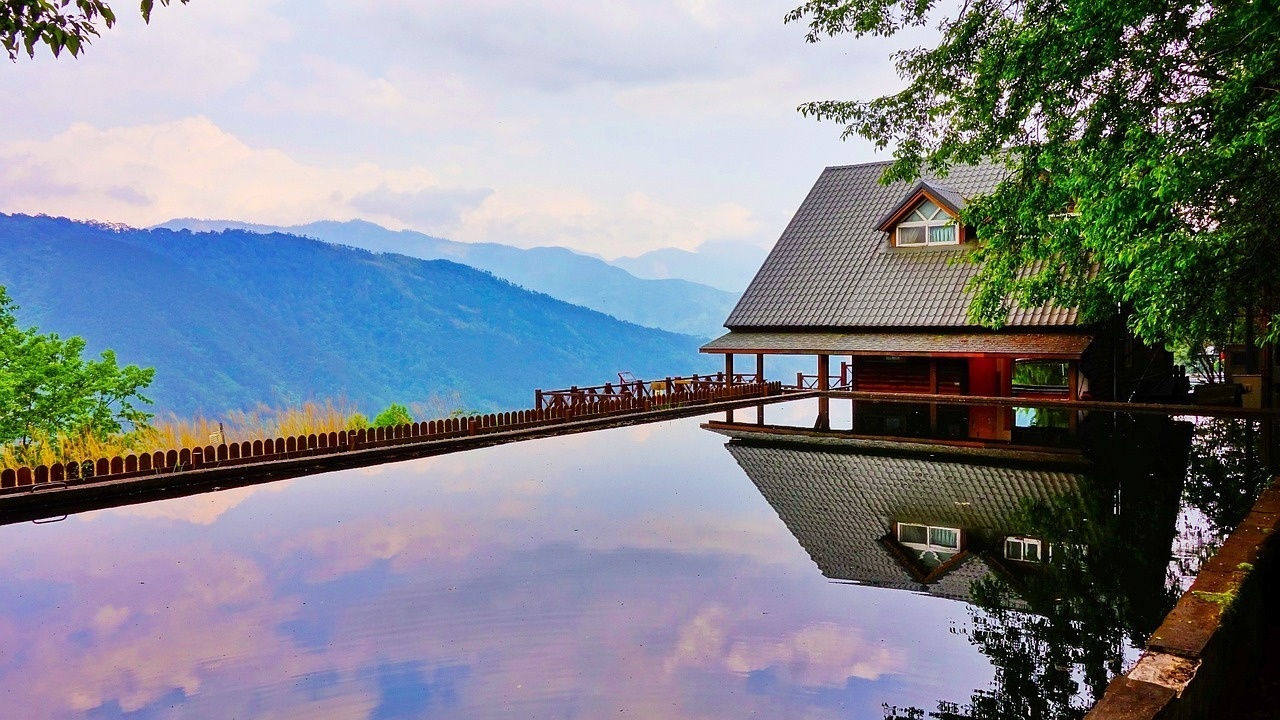 a house is reflected in a body of water with mountains in the background