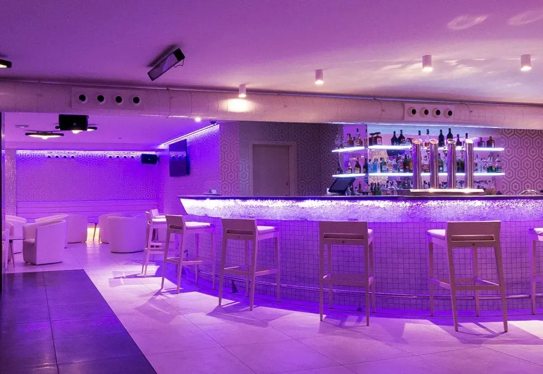 Bar moderno del Hotel ESTIVAL: Park Silmar con iluminación púrpura y taburetes.