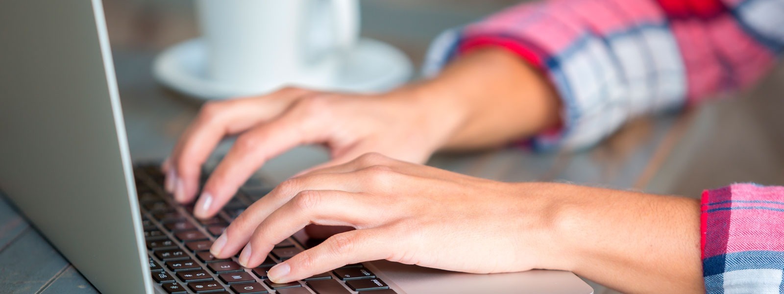 a person typing on a laptop with a cup of coffee in the background