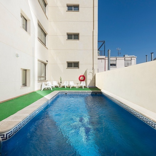 una pequeña piscina rodeada de sillas y un edificio blanco